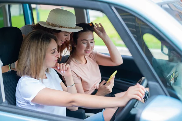 Tre lyckliga flickvänner åker på en resa. Kvinnor Rida i bilen, titta på telefonen och skratta. — Stockfoto