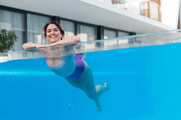 Mujer caucásica feliz nada en una piscina al aire libre con una pared transparente en un hotel —  Fotos de Stock