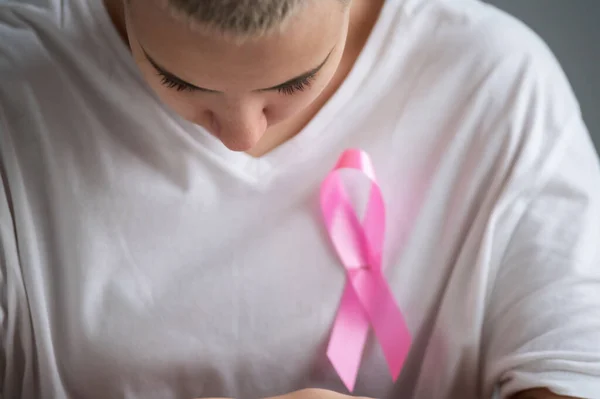 Mulher com um corte de cabelo loiro curto com uma fita rosa em uma camiseta branca como um símbolo de câncer de mama em um fundo branco. — Fotografia de Stock