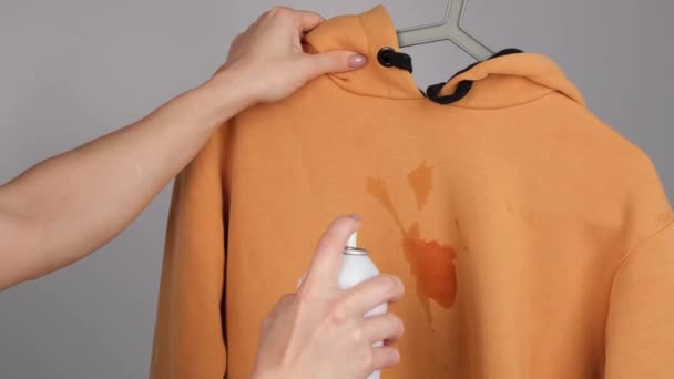 Una mujer usa un spray quitamanchas en una sudadera con capucha de ocre — Vídeo de stock