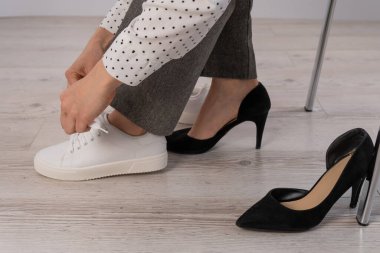 Yakın plan iş kadını ayakkabılarını çıkarıp beyaz deri ayakkabılarını giyer..