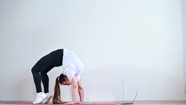 Une jeune femme flexible se tient debout sur le pont et mène un cours de gymnastique à distance sur un ordinateur portable. — Video