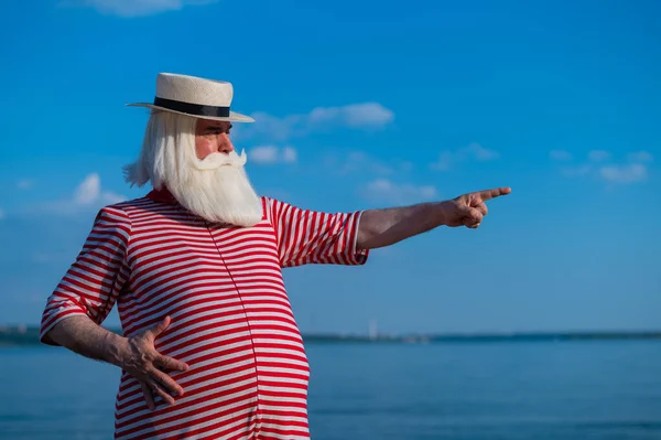 Пожилой человек в полосатом ретро-купальнике и лодке на берегу моря — стоковое фото