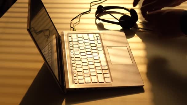 L'uomo prende le cuffie dalla tastiera del computer portatile e inizia a digitare — Video Stock