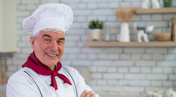 Portrét usměvavého staršího kuchaře stojícího v kuchyni se zkříženýma rukama na prsou. — Stock fotografie