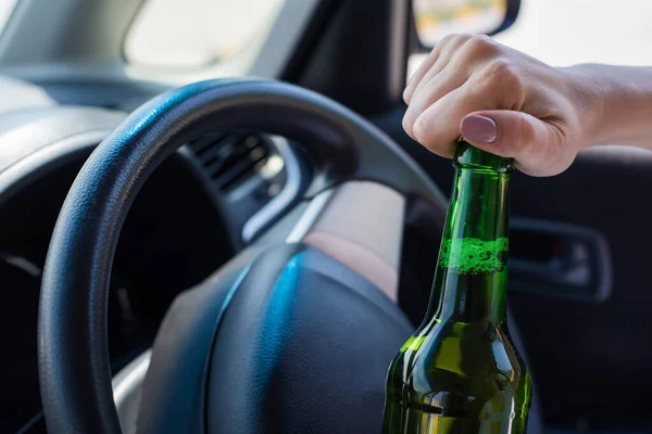 Una mujer sin rostro abre una botella de cerveza mientras conduce un coche. Violar la ley y beber alcohol mientras conduce — Foto de Stock