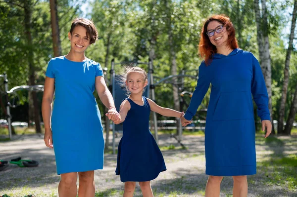 Гомосексуальная лесбийская пара держит дочерей за руки. Девушка гуляет с двумя матерями в парке. Две замужние женщины и ребенок на улице. — стоковое фото
