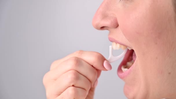 Кавказька жінка чистить зуби зубочисткою з зубною ниткою на білому тлі.. — стокове відео