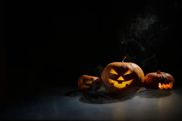 Calabazas con muecas talladas y velas en el interior en la oscuridad para Halloween. Jack o latern en el humo. — Foto de Stock