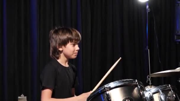 Мальчик учится играть на барабанах в студии на чёрном фоне. Студентка музыкальной школы — стоковое видео