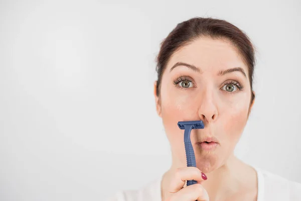 Mujer divertida caucásica se afeita la cara con una navaja de afeitar sobre un fondo blanco. Copiar espacio. — Foto de Stock