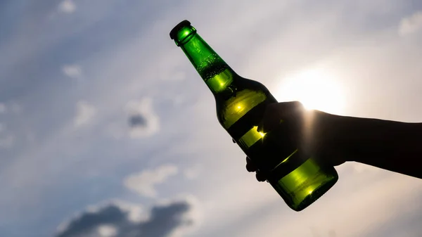 Женщина держит бутылку пива на открытом воздухе на фоне неба. — стоковое фото
