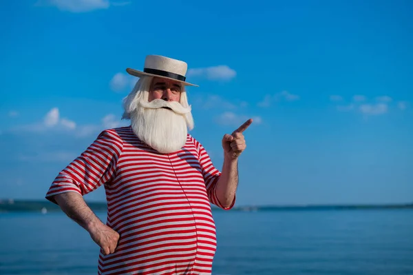 Пожилой человек в полосатом ретро-купальнике и лодке на берегу моря — стоковое фото