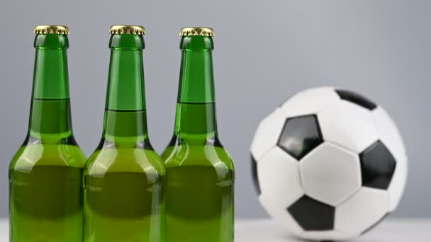 Uma bola de futebol está girando ao lado de três garrafas de cerveja em um fundo branco — Vídeo de Stock