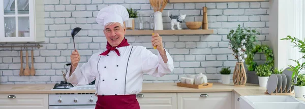 Portrét usměvavého staršího kuchaře, jak ochutnává lopatkový talíř v kuchyni. — Stock fotografie