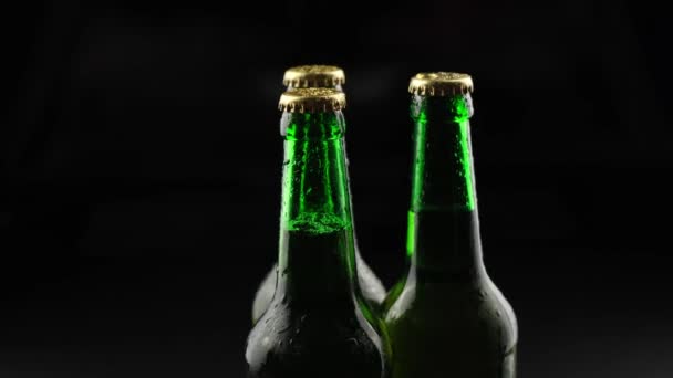 Tre bottiglie di birra di vetro verde che girano su uno sfondo nero al buio — Video Stock