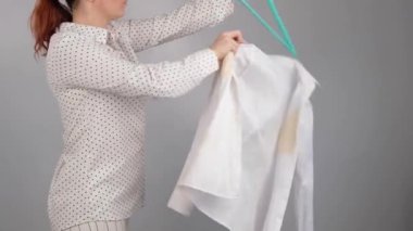 Bir kadın, beyaz gömleğini askılarındaki kahve lekesiyle çıkarıp atıyor. Bozuk kıyafetler.