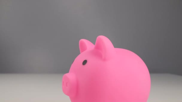 Faceless caucasian woman folds a small heart into a pink piggy bank on a white background. Love saving concept — Stock Video