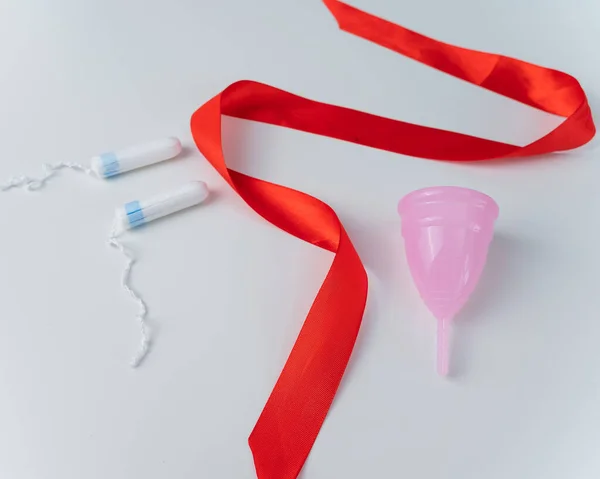 Tampão, xícara menstrual rosa e fita de cetim vermelho em um fundo branco. Meios de higiene íntima de uma mulher durante a mentruação — Fotografia de Stock