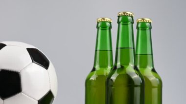 Bir futbol topu beyaz arka planda üç şişe biranın yanında dönüyor.