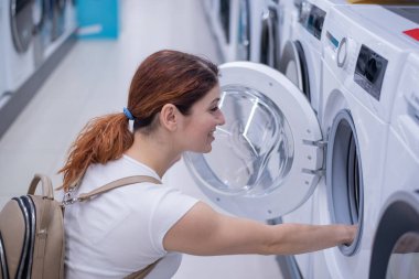 Beyaz kadın ev aletleri mağazasından çamaşır makinesi seçiyor.