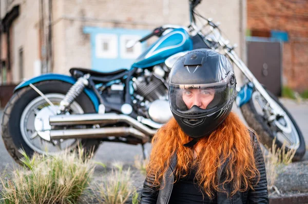 Rödhårig lockig kvinna i hjälm nära motorcykel. — Stockfoto