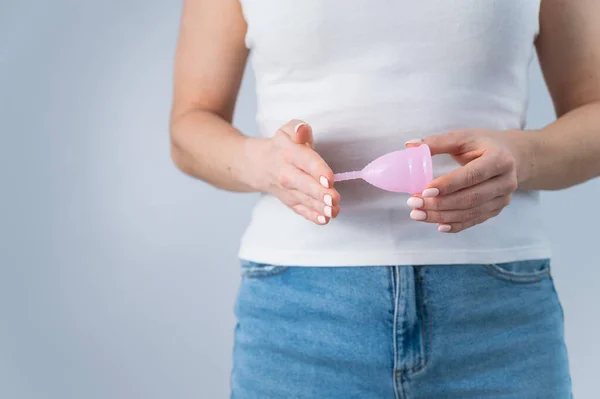 Een gezichtloze vrouw in jeans en een wit T-shirt heeft een roze menstruatiecup op een witte achtergrond. Geweldig alternatief voor tompons en pads — Stockfoto