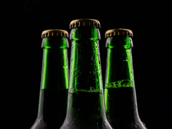 Три бутылки пива из зеленого стекла на черном фоне. — стоковое фото