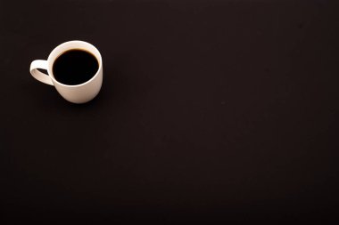 Beyaz seramik fincanın siyah arka planda koyu kahve ile üst görüntüsü. Boşluğu kopyala