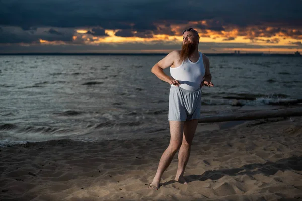 En brutal skallig man poserar på stranden vid solnedgången parodi glamorös brud — Stockfoto