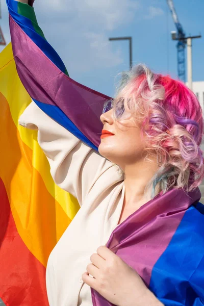 Mulher caucasiana com cabelos encaracolados segurando bandeira lgbt. Mulher lésbica segurando uma bandeira do arco-íris ao ar livre — Fotografia de Stock