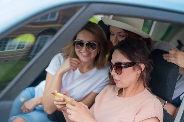 Tre lyckliga flickvänner åker på en resa. Kvinnor kör bil och tar en selfie på en mobiltelefon — Stockfoto