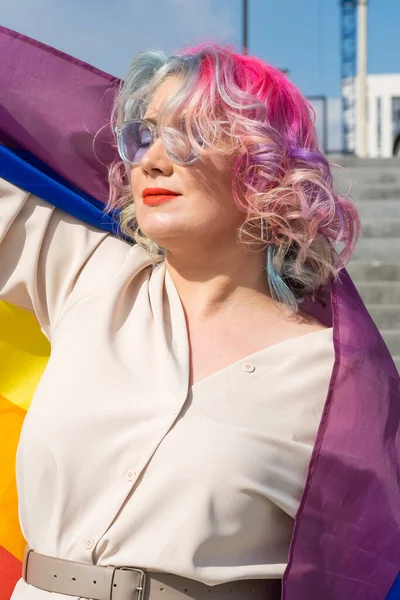 Mujer caucásica con cabello rizado con bandera lgbt. Mujer lesbiana sosteniendo una bandera de arco iris al aire libre —  Fotos de Stock