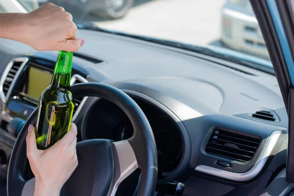 A faceless woman opens a bottle of beer while driving a car. Breaking the law and drinking alcohol while driving