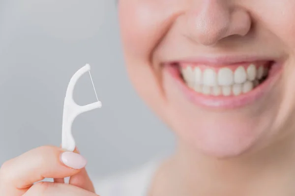 Close-up retrato de uma bela mulher caucasiana com um sorriso impecável segurando um palito com fio dental em um fundo branco — Fotografia de Stock