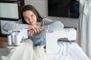 Genç beyaz kadın evde dikiş dikiyor.