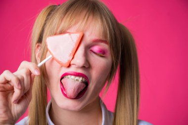 Pembe arka planda lolipop yiyen parlak makyajlı genç bir kadının portresi..