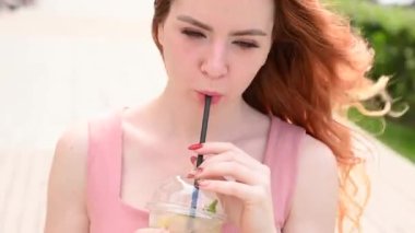 Diş teli takan güzel, kızıl saçlı bir kadın yazın dışarıda soğuk limonata içiyor. Çilli, gülümseyen bir kızın portresi..
