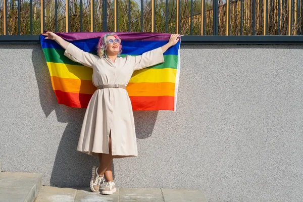 Mujer caucásica con pelo rizado sosteniendo bandera lgbt contra una pared gris. Mujer lesbiana sosteniendo una bandera de arco iris al aire libre —  Fotos de Stock