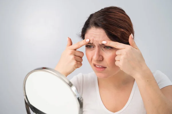 Mujer caucásica se mira en el espejo y está molesta debido a las arrugas faciales en su cara. — Foto de Stock