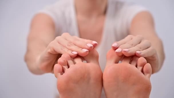 Primer plano de una mujer aplicándose crema en los pies y masajeando sus dedos sobre un fondo blanco — Vídeos de Stock