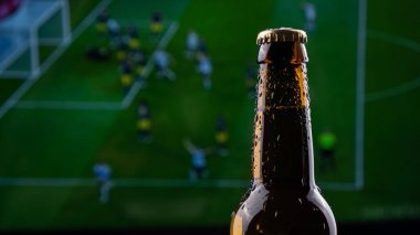 Bir futbol maçı yayınının arka planında bir şişe bira..