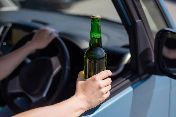 Una mujer sin rostro está bebiendo una botella de cerveza mientras conduce un coche. Violar la ley y beber alcohol mientras conduce — Foto de Stock