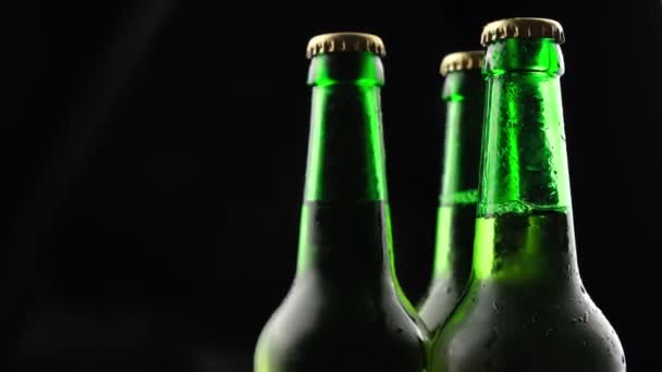 Tres botellas de cerveza de vidrio verde girando sobre un fondo negro en la oscuridad — Vídeo de stock