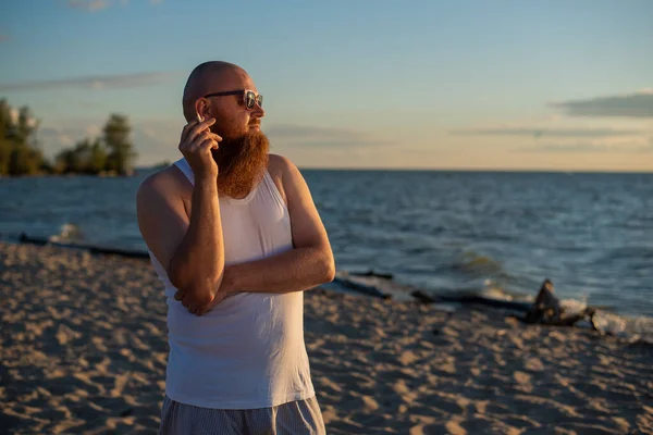 Brutale uomo barbuto fuma una sigaretta sulla spiaggia. La cattiva abitudine porta al cancro — Foto Stock