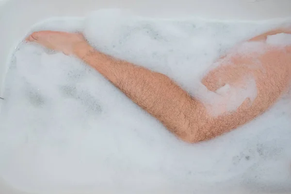 Divertida foto de un hombre tomando un baño relajante. Primer plano de los pies masculinos en un baño de burbujas. Vista superior —  Fotos de Stock