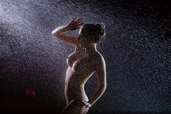 A beautiful European nude woman under sprinkler at night.