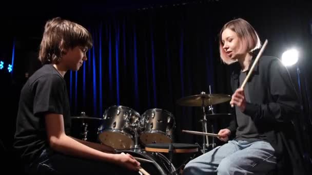 Νεαρή λευκή γυναίκα διδάσκει σε ένα αγόρι να παίζει ντραμς στο στούντιο σε μαύρο φόντο. Μαθητής μουσικής σχολής — Αρχείο Βίντεο