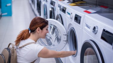 Beyaz kadın ev aletleri mağazasından çamaşır makinesi seçiyor.