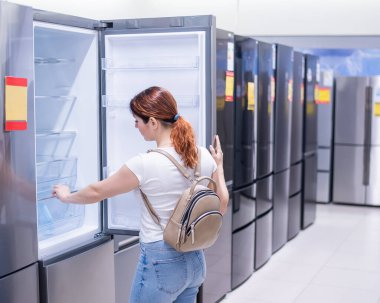 Beyaz kadın bir ev aletleri dükkanından buzdolabı seçiyor.